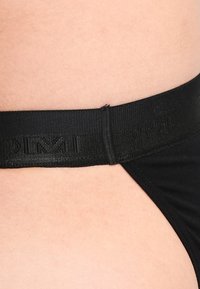 Slip nero con una finitura liscia e opaca e una cintura larga con logo. Mostra la texture della pelle lungo il bordo e l'area della cintura.