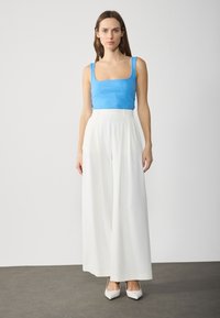 Top sin mangas azul de canalé con escote cuadrado, combinado con pantalones blancos de cintura alta y pierna ancha, y tacones blancos puntiagudos. Tela suave, diseño minimalista.