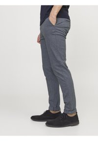 Gray patterned trousers with a slim fit, featuring side pockets and a rolled hem, paired with black suede shoes.