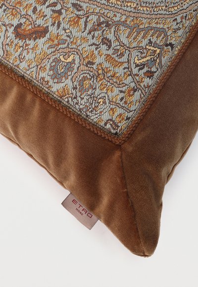 Coin d'un coussin en velours marron avec un motif floral et cachemire tissé, et une étiquette en tissu indiquant "ETRO HOME" sur fond blanc.