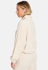 Ribbed, cremefarbene Sweatshirt mit hohem Kragen, entspannter Passform und tief sitzenden Schultern, kombiniert mit passenden Hosen.
