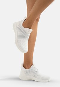 Scarpe sportive bianche in materiale mesh, con cinturini elastici, lati texturizzati e soletta ammortizzata, progettate per comfort e flessibilità.