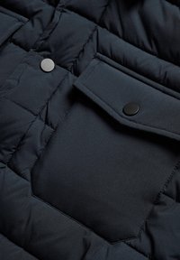 Mornarska puffer jakna iz tkanine z gubicami, z zloženo žepom in okroglicami črne barve. Gladek zaključek z elegantnim dizajnom.