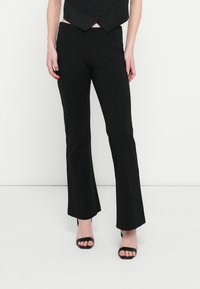 Mustad laienevad püksid siledast kangast, keskmise kõrgusega vöökohaga ja keha järgiva lõikega, kombineeritud mustade rihmikandadega kontsadega.