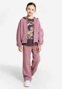 Liliowa bluza z kapturem na zamek, w zestawie z t-shirtem z grafika na przodzie, dopasowanym do szerokich spodni i białych sneakersów. Miękka faktura materiału.