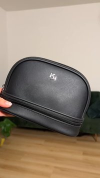 Schwarze kosmetische Tasche aus synthetischem Material mit strukturierter Oberfläche, abgerundetem Oberteil, silbernem Reißverschluss und Logo auf der Vorderseite. Maße ca. 20x13 cm.