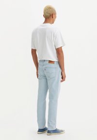 Lichtblauwe denim jeans met een rechte fit, leren patch op de achterkant van de tailleband en subtiele stiksels. G gedragen met een wit T-shirt en blauwe sneakers.