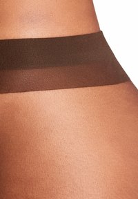 Brązowe półprzezroczyste rajstopy o gładkiej fakturze i szerokim ciemno-brązowym pasie. Materiał ma lekki połysk i zlewa się z odcieniami skóry.