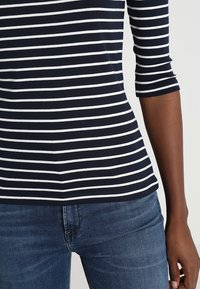 Navy blue and white striped long-sleeve top made of soft fabric. Fitted design with a round neckline and three-quarter sleeves.