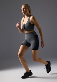 Sostén atlético gris y pantalones cortos con acentos negros, que presentan un diseño ajustado y una textura suave, combinados con zapatillas de correr negras.