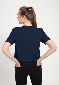 Námořnická modrá tričko s krátkým rukávem a kulatým výstřihem, vyrobené z měkké látky, s uvolněným střihem a jemnými stehmi. Nosené s černými džíny.