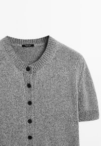 Maglione grigio a maniche corte in maglia con scollatura rotonda, caratterizzato da cinque bottoni neri sulla parte anteriore e una superficie testurizzata.