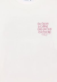 Biała koszulka z różowym napisem z przodu "Ocean wzywa, jest tylko jeden sposób, do widzenia" oraz małymi znaczkami o tematyce podróżniczej.