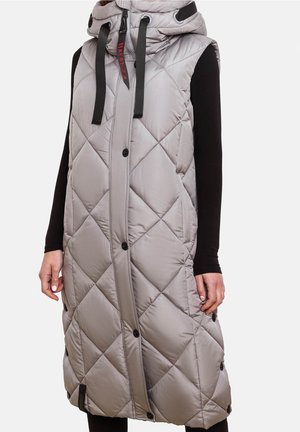 Manteau long matelassé gris sans manches avec capuche, cordons noirs, boutons sur le devant, porté par-dessus un haut noir à manches longues.