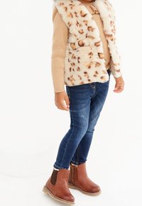 Fauxpälsväst med bruna leopardfläckar, tanfärgad stickad tröja, blå denimjeans och bruna ankelstövlar med scallopdetaljer.