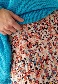 Knitted turquoise sweater overlaying a floral-patterned skirt with a smocked waistband. Dominant colors are pink, red, and navy.