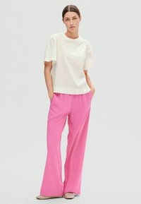 White short-sleeve top with textured fabric, paired with wide-leg pink pants. The outfit features relaxed fit and side pockets.