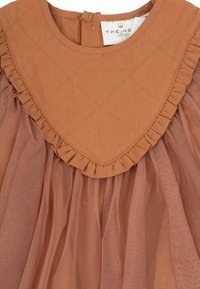 Rūsganas kokvilnas kleitas ar quilted krūšu daļu, viļņotu apkakli un caurspīdīgu tilla svārku, kas ir kārtota zemāk. Tekstūrētas auduma detaļas.