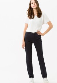 Pantaloni neri slim fit, con chiusura a bottone e tasche frontali, abbinati a una maglietta bianca a maniche corte e sneakers bianche.