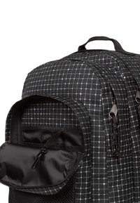 Mochila negra con un patrón de cuadrícula en tonos grises. Incluye un bolsillo frontal con cremallera y tejido texturizado. Asa resistente en la parte superior.