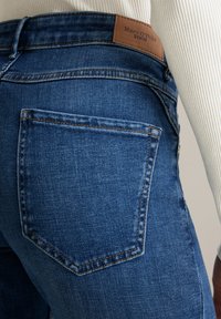 Dunkelblaue gerade geschnittene Jeans aus Denim, mit einer Gesäßtasche und einem beigefarbenen Lederetikett am Bund mit dem eingeprägten Schriftzug "Marc O'Polo DENIM".