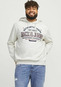Hanorac gri deschis cu un grafic frontal care prezintă "Jack & Jones" în roșu închis și bleumarin. Cu glugă cu șnururi și buzunar tip kangaroo. Purtați cu blugi albaștri.
