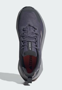 Chaussures de sport gris foncé avec tige en maille, embout renforcé, semelle texturée et intérieur rouge contrasté. Comprend une languette à l'arrière.