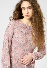 Helles rosafarbenes Kleid mit aufwendigen Paillettenmustern, langen Ärmeln und gerafften Manschetten. Verfügt über geometrische Designs und eine strukturierte Oberfläche.