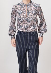 Blouse à manches longues avec un motif paisley coloré dans des nuances de bleu et de rose, dotée d'un design en trou de serrure au niveau du cou, associée à un pantalon rayé navy.