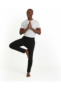 Lichtgrijs shirt met korte mouwen en zwarte joggers met een elastische tailleband. De joggers hebben een subtiele logo op het linkerbeen.