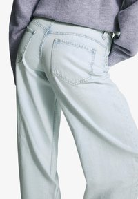 Svijetloplave široke traperice izrađene od denima, s pet džepova, suptilnim šavovima i opuštenim krojem. Tekstura tkanine je blago izblijedjela.