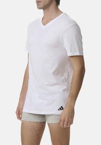 White cotton v-neck t-shirt with short sleeves, featuring a black Adidas logo on the bottom left. Smooth texture and casual design.