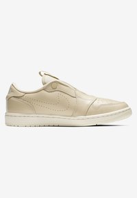 Beige Leder-Sneaker mit einem Slip-On-Design, das subtile Perforationen, eine weiße Sohle und ein seitliches Logo-Detail aufweist. Glatte Textur überall.