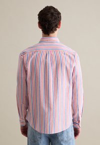 Camisa de manga larga en rayas verticales azules, rojas y blancas. Cuenta con un cuello con punta, puños abotonados y un dobladillo curvo. Detalle de yugo en la parte de atrás visible.