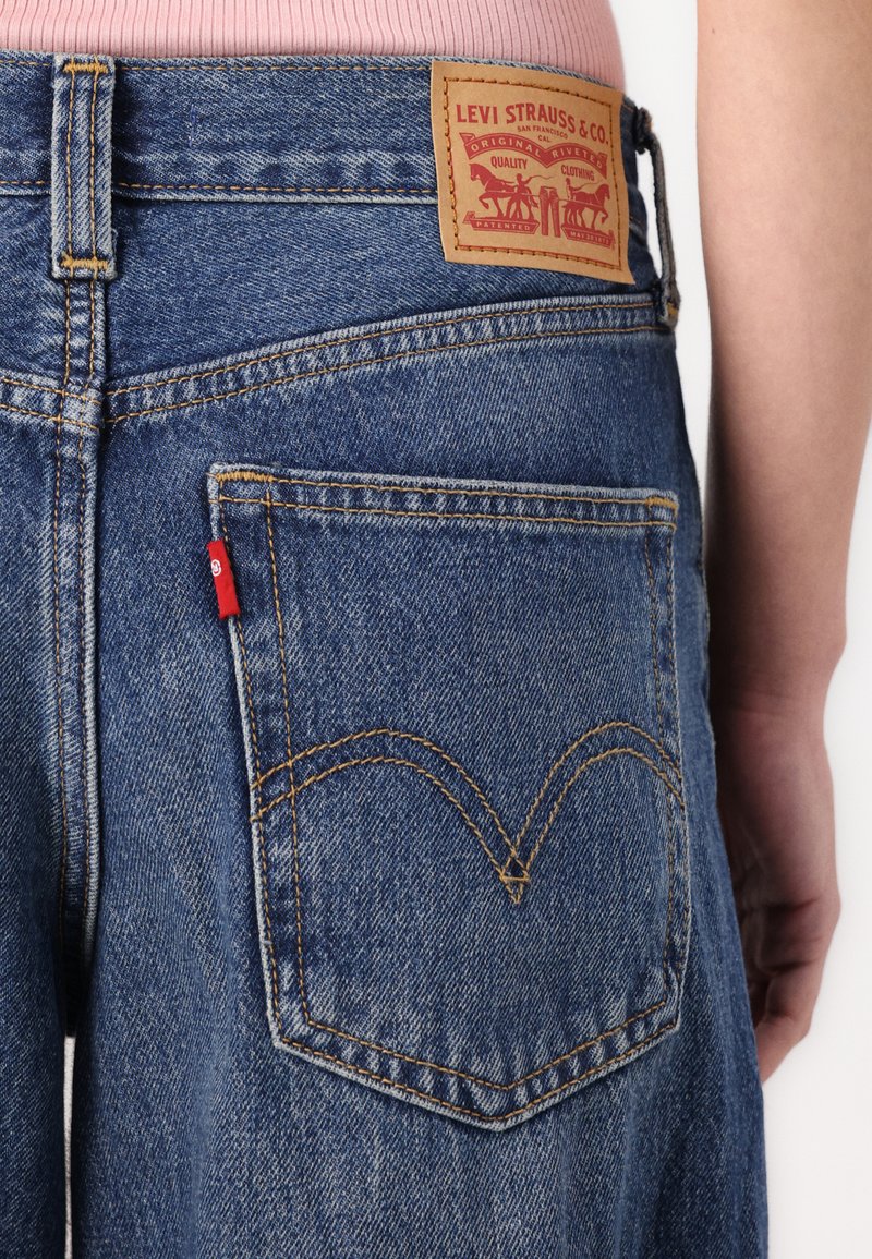 Achteraanzicht van een blauwe denim jeans van Levi's met een oranje stiksel en een leren merklabel boven de tailleband.