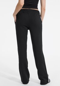 Black sweatpants made of soft fabric, featuring a relaxed fit, elastic waistband, side pockets, and white stripes along the legs.
