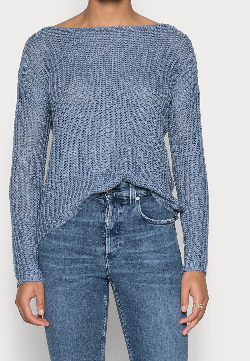 Pull en tricot bleu clair avec une coupe ample, un col large et un tissu texturé. Associé à un jean en denim bleu ajusté.
