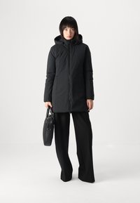 Zwarte gewatteerde parka met een capuchon, een ritssluiting aan de voorkant en een slanker silhouet. Gepaard met zwarte wijde broek en een gestructureerde zwarte tas.