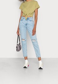 Khaki skrócony t-shirt z węzłowym detalem, jasnoniebieskie zniszczone dżinsy oraz mała torebka w paski. Całość dopełniają białe i żółte sneakersy.