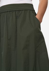 Ciemnozielona spódnica wykonana z lekkiego materiału. Posiada elastyczną talię oraz boczne kieszenie, a jej powierzchnia jest miękka i lekko pofałdowana.