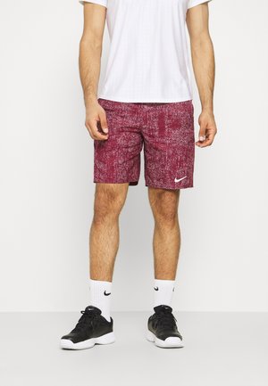 Shorts deportivos color burdeos con un patrón texturizado, con un logo de Nike en blanco. Combinados con una camiseta de patrón a cuadros en blanco y zapatillas negras.
