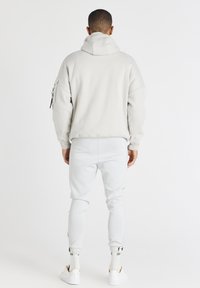 Felpa grigia chiaro con colletto alto, vestibilità ampia e tasca con zip sulla manica sinistra. Abbinata a pantaloni tuta bianchi a gamba affusolata e sneakers.