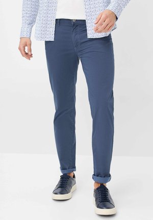 Navy blue cotton chinos with a slim fit, showcasing a smooth texture and rolled cuffs. Paired with dark blue sneakers.