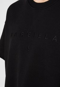 Sudadera negra con cuello redondo, mangas cortas y texto bordado tonal "MARGIELA" y el número "6" en la parte frontal.