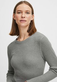 Maglione grigio a coste con maniche lunghe e scollatura rotonda, caratterizzato da una texture morbida e un design aderente.