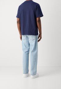 Marineblå kortærmet t-shirt parret med lyseblå løstsiddende jeans og hvide sneakers. Stoffet fremstår glat med en afslappet silhuet.