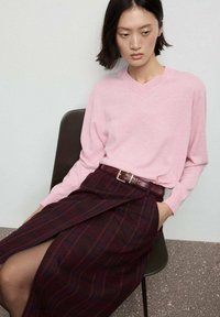 Jasnoróżowy sweter w serek z długimi rękawami, zestawiony z ciemnofioletową spódnicą w kratkę, z paskiem z metalową klamrą.