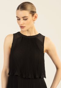 Schwarzes, plissiertes Kleid mit ärmellosem Design, Rundhalsausschnitt und schichtweise fallendem Saum. Die glatte Textur verstärkt den fließenden Stoff.
