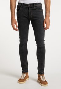 Jeans de denim negro ajustados con un ligero desgaste, cinco bolsillos y costuras en contraste, combinados con zapatillas altas de ante marrón.