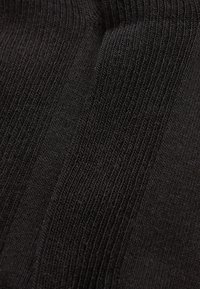 Schwarzer Strickstoff mit vertikaler Rippstruktur. Das Material ist dehnbar und dicht und zeigt Variationen in der Strickdichte.